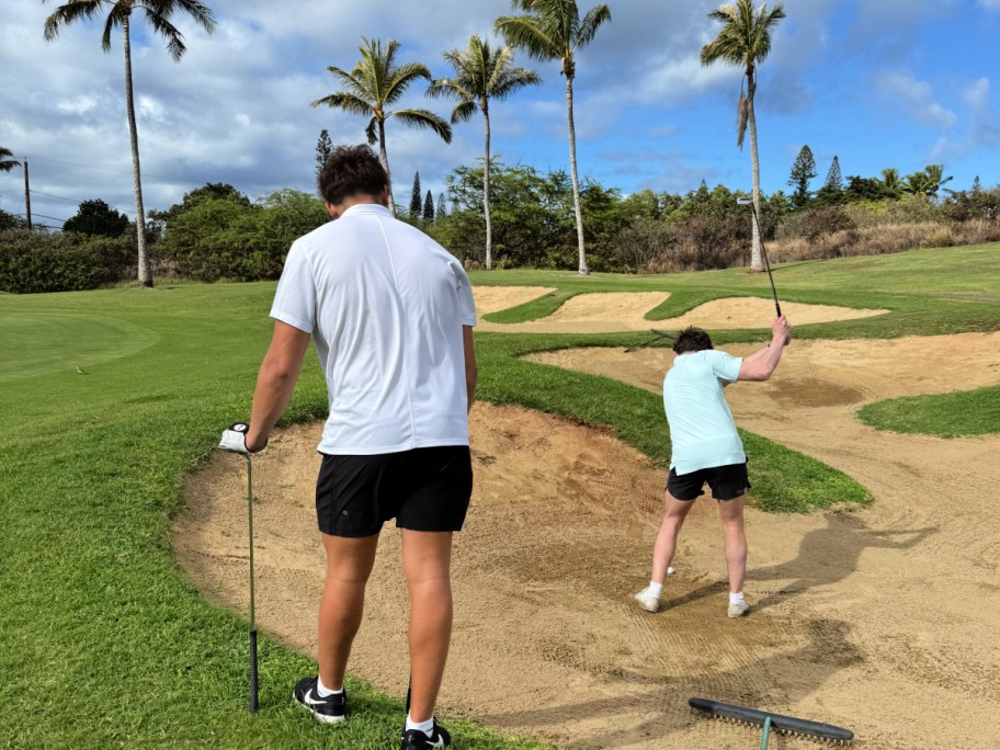Two boys golfing surrounded by palm trees