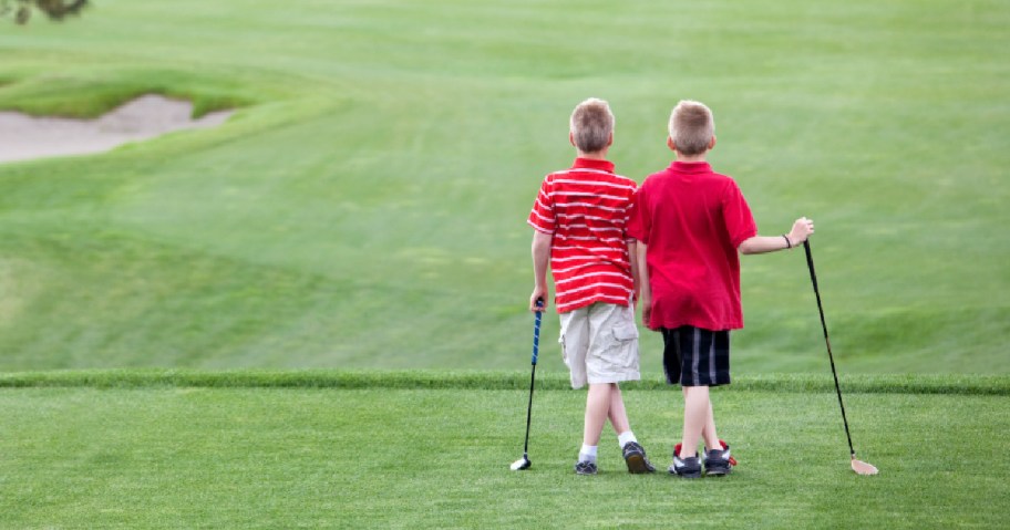 Two young boys standing on golf course, each holding a golf club in their hands