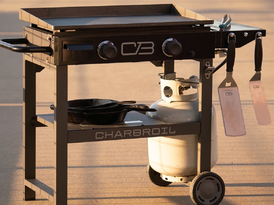charbroil griddle outside with grill accessories hung up, a propane tank and pots on its self