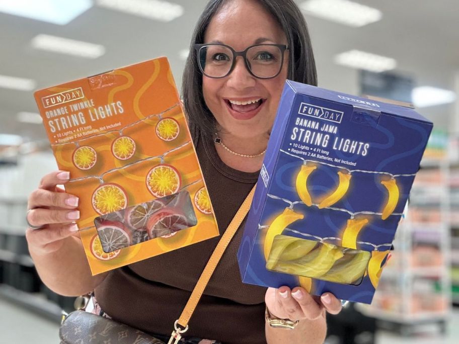 A woman holding two boxes of fruit-shaped string lights at Target