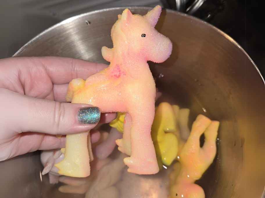 hand holding a toy unicorn over a bowl with more in it