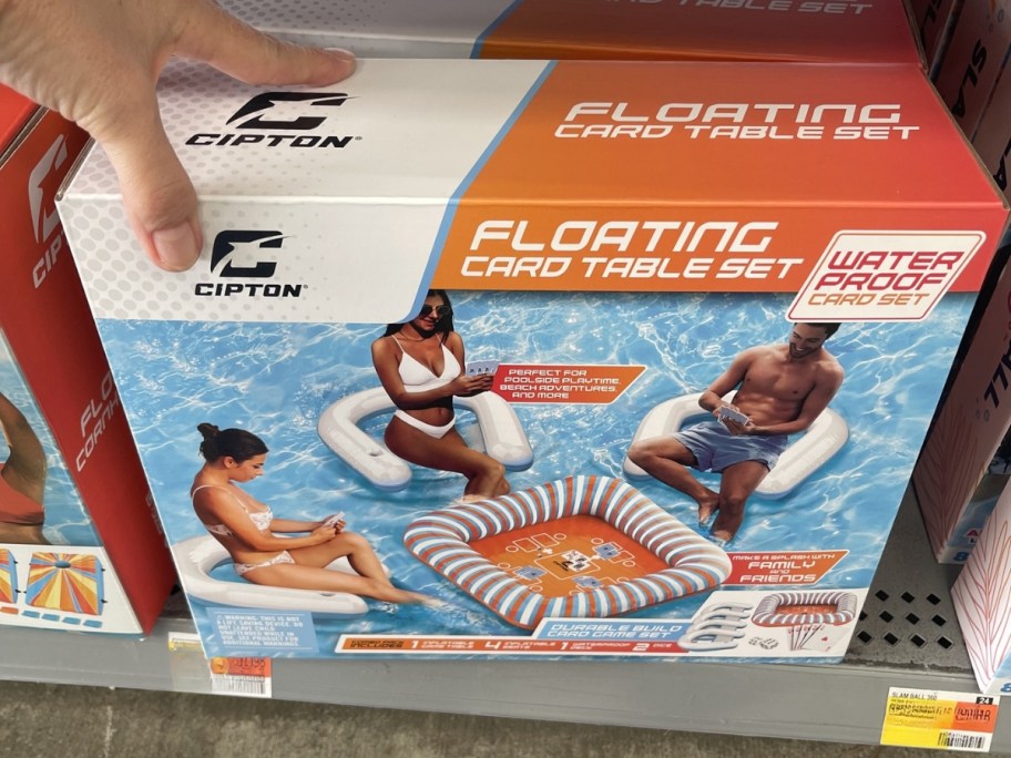 hand reaching for a box with an Inflatable Card Table Set with Seats set in it on store shelf