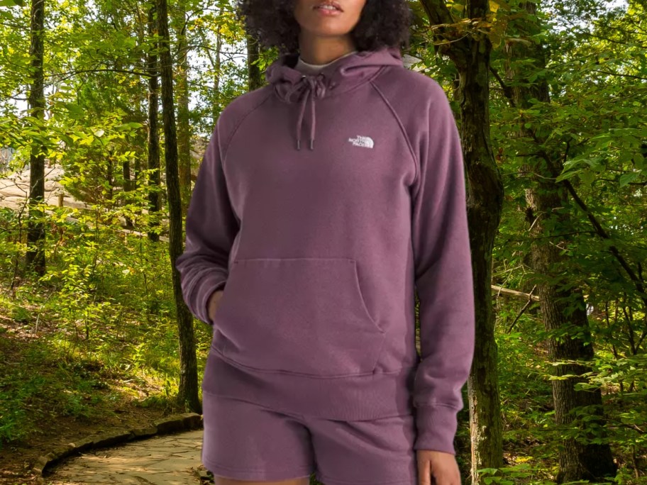 woman in a purple The North Face Hoodie standing in the woods by a trail