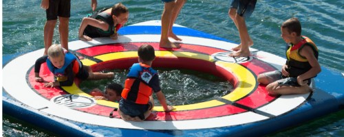 bunch of kids in the middle of a lake playing on a large water pad