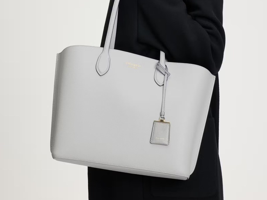 Person carrying a light gray Kate Spade Suite Large Work Tote with top handles and a matching luggage tag charm.