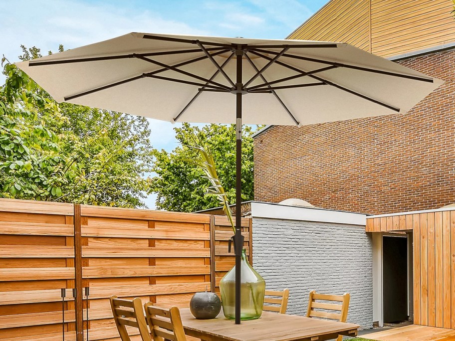 outdoor umbrella displayed on top of a patio set with a wooden gate in the background