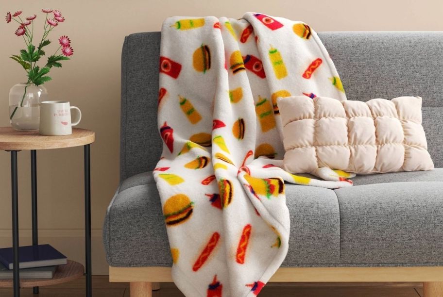 a throw with hamburger, and hot dog graphics printed all over. the throw is shown draped over a sofa