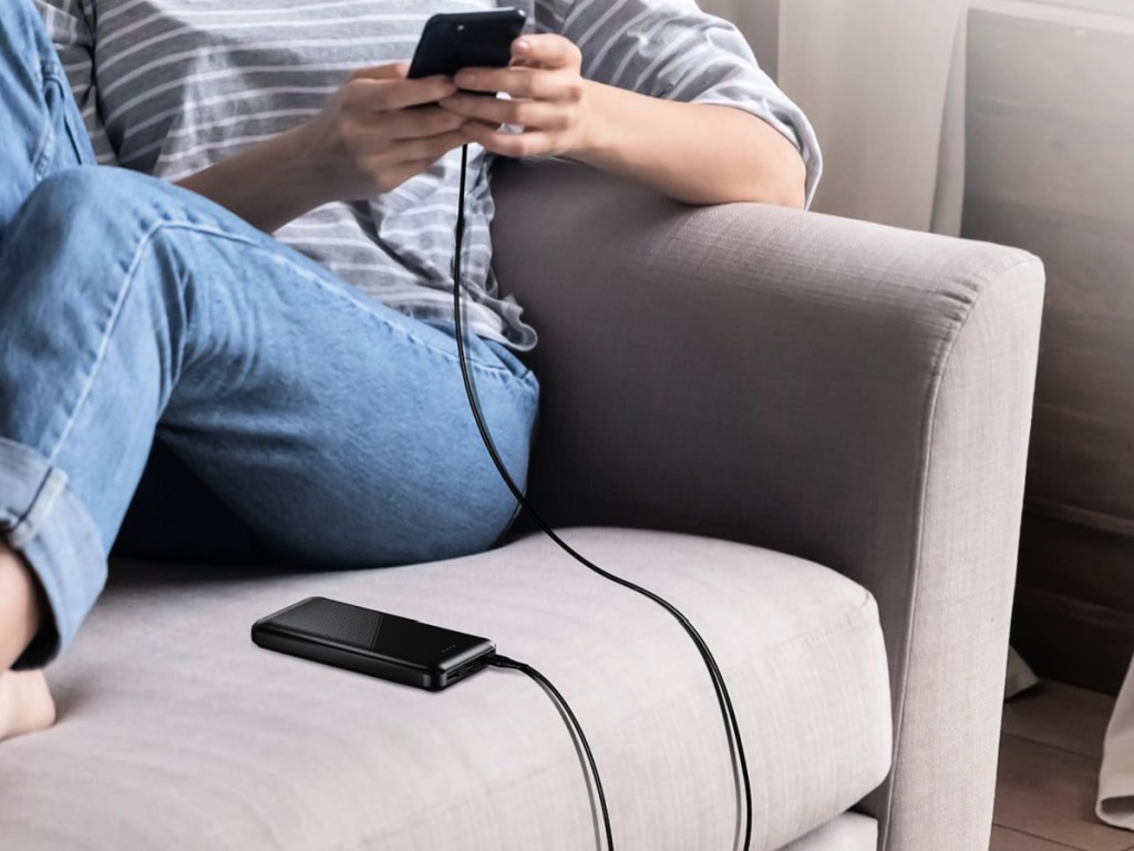 woman charging black phone with portable charger on couch