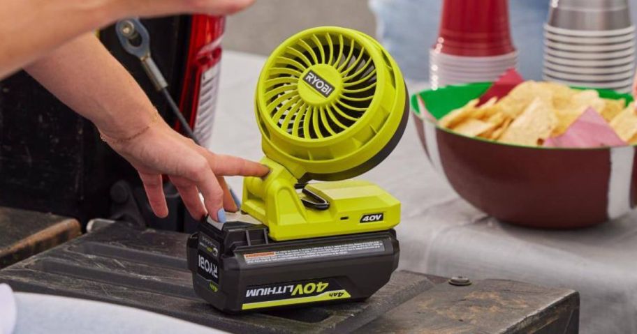 A person adjusting a RYOBI fan during a picnic