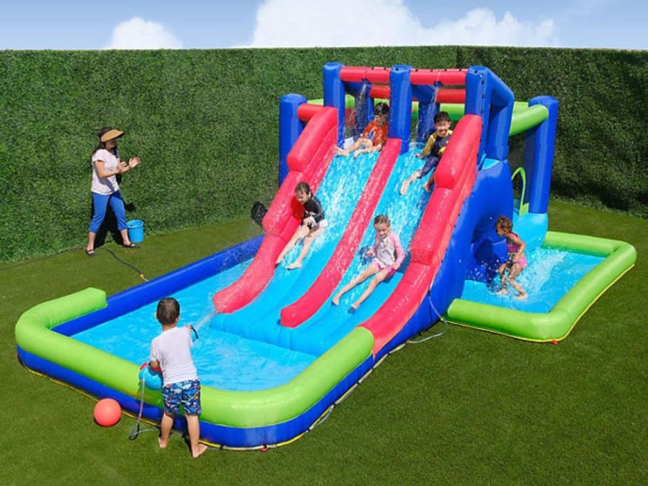 Multiple children playing on a My 1st Water Slide Giant Water Park Play Center with a female adult watching nearby