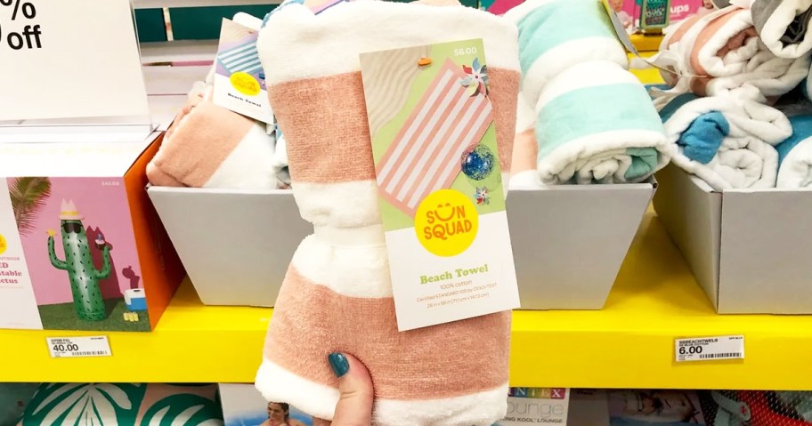 hand holding up a pink and white striped beach towel in store