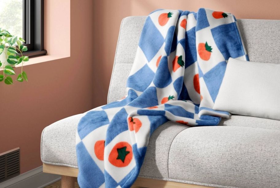 a throw with tomato and checkerboard graphics printed all over. the throw is shown draped over a sofa