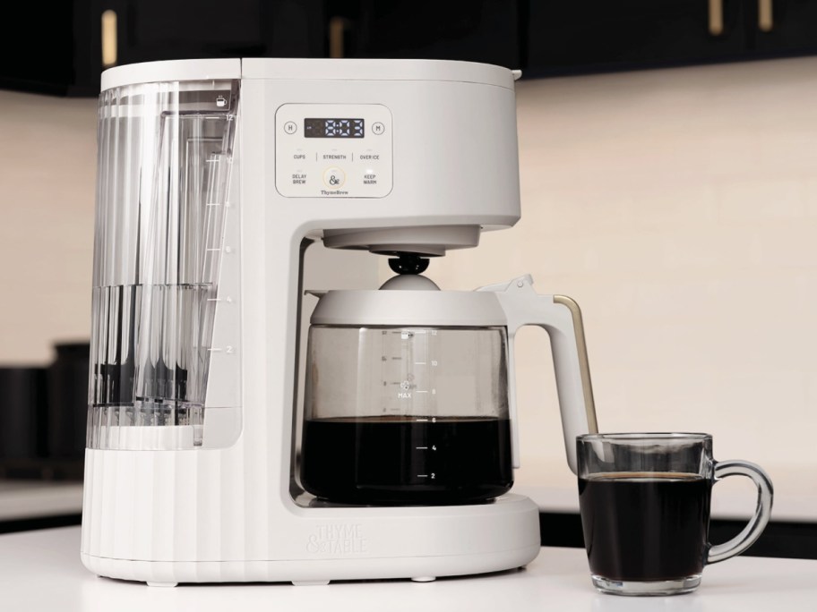 Thyme and table drip coffee machine displayed on top of the table with a cup of coffee next to it