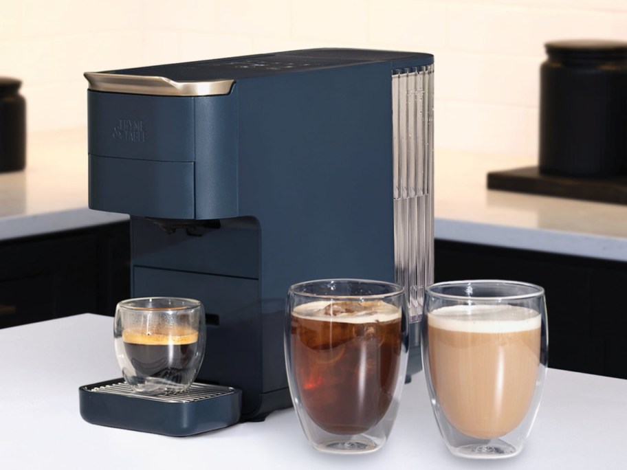 Navy blue thyme and table capsule coffee maker with three different coffee types next to each other