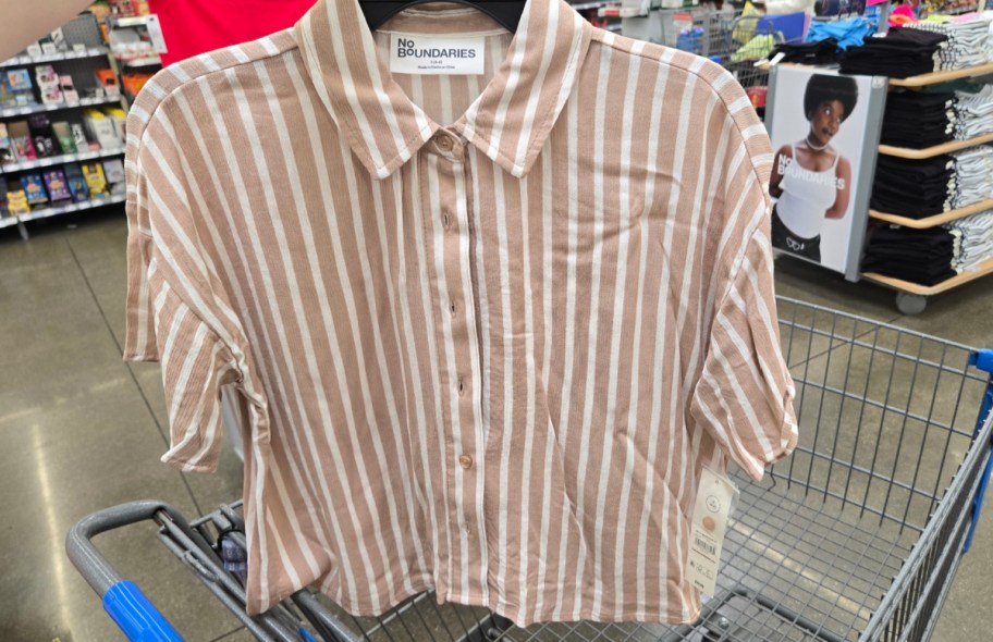 hand holding up shirt set in front of a walmart cart