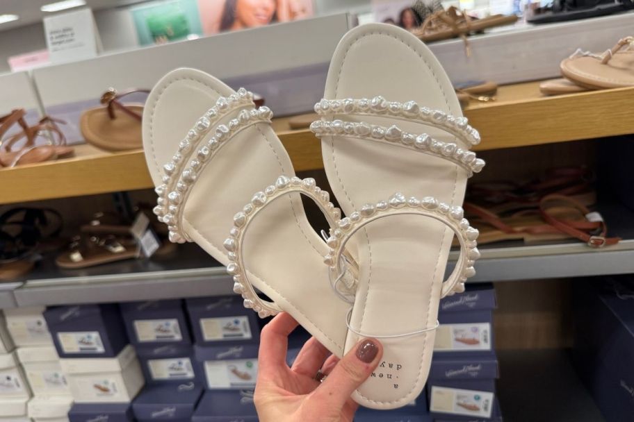 a womans hand holding a pair of white strappy low heeled slide sandals