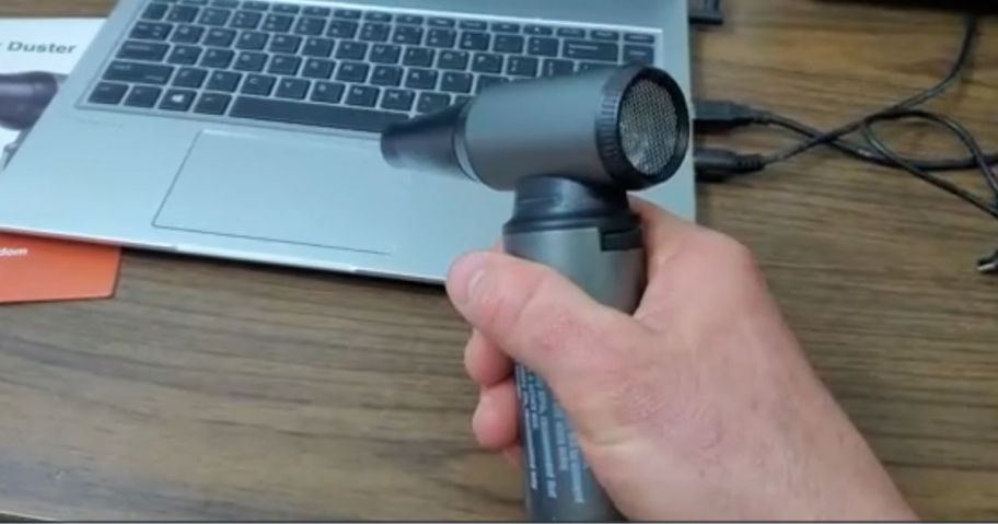 hand holding black compressed air duster to blow dust away from laptop