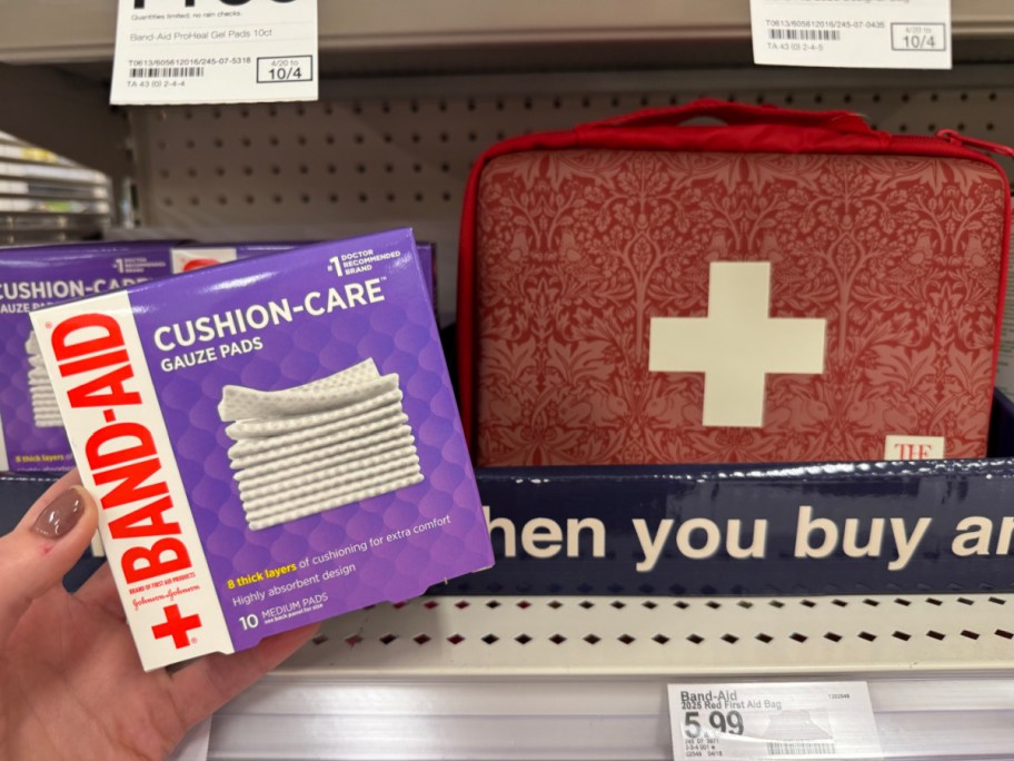 hand holding a box of gauze pads near a first aid kit in a store