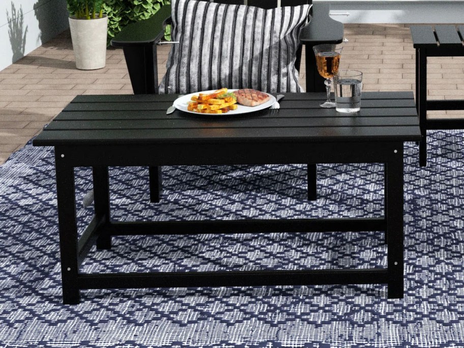 black coffee table with plate of food and drinks on top 
