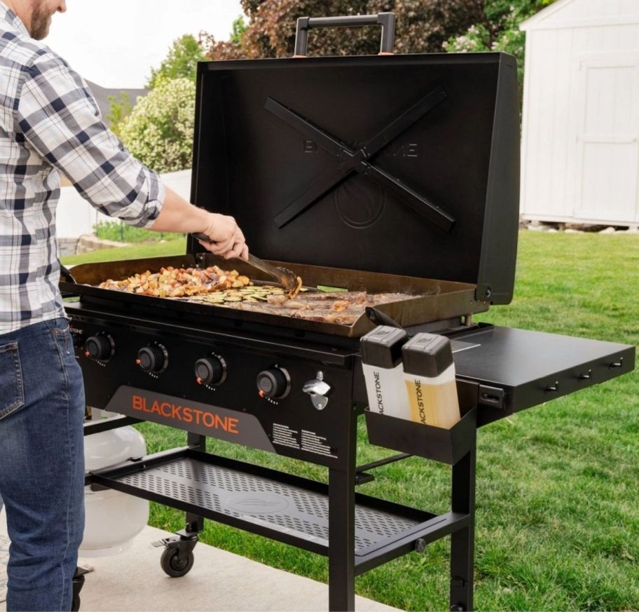 a man turning meat as it cooks on a large black outdoor griddle