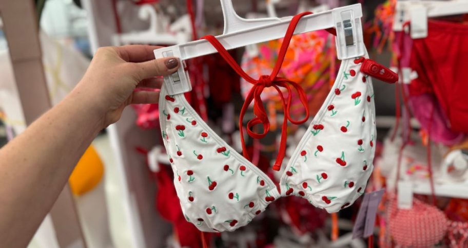 hand holding a cherry print bikini top in front of a store display of swimwear