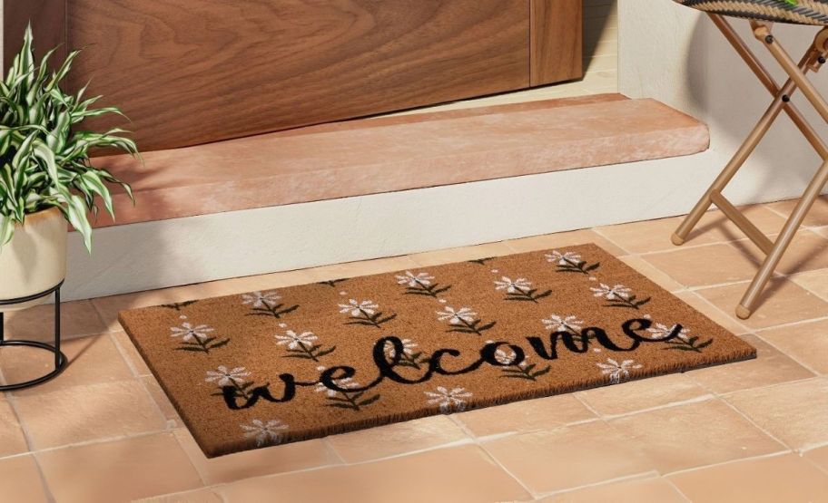 a coir doormat with a black and white floral print in front of a wooden door