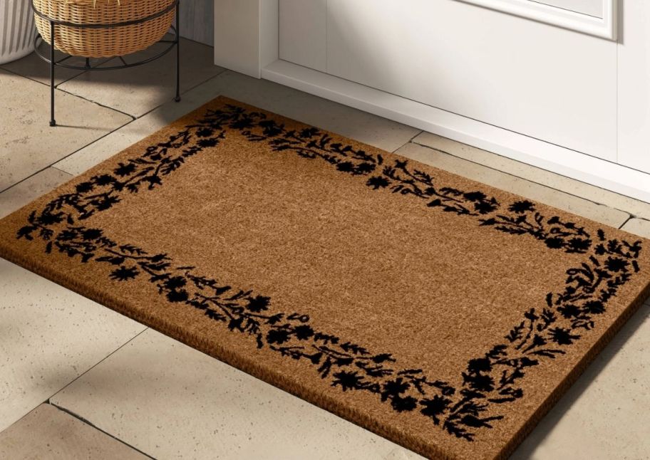 a coir doormat with a black floral border infront of a white door