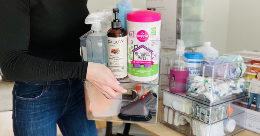 woman holding up clear plastic bins full of cleaning products