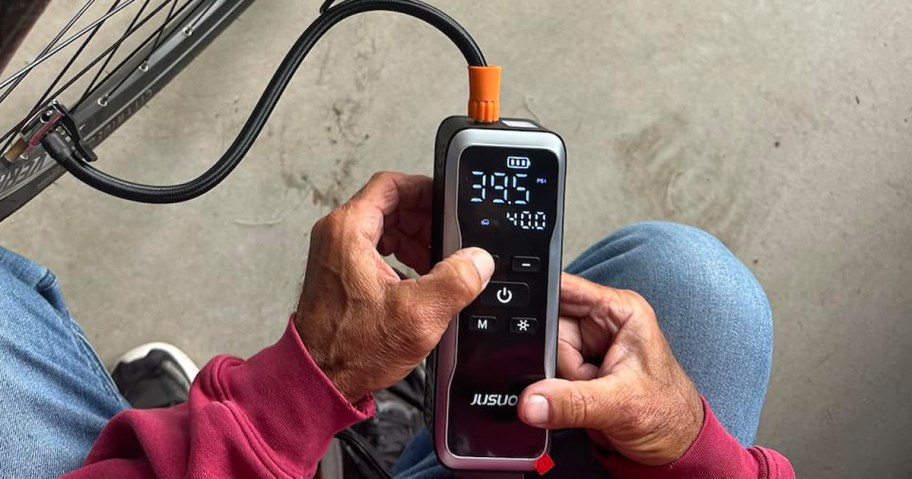 man holding a portable tire compressor to inflate a bike tire
