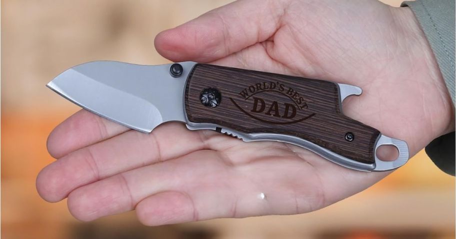 hand holding Wood Folding Knife with world's best dad engraved on it