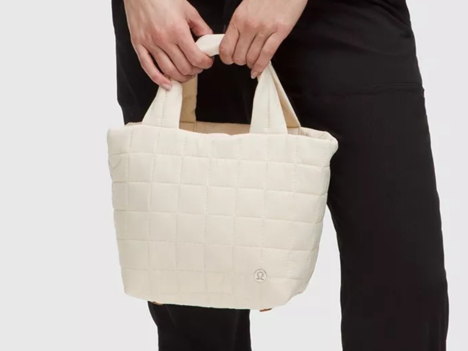 lower half of a woman holding a cream quilted styles handbag