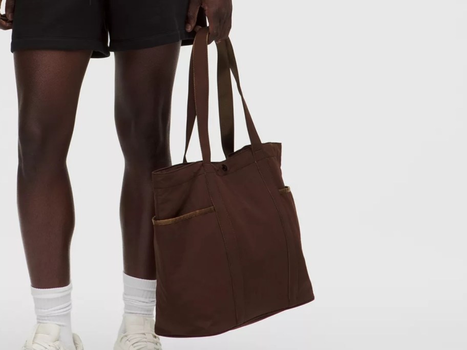 lower half of a man, he is holding a large brown tote bag by his leg