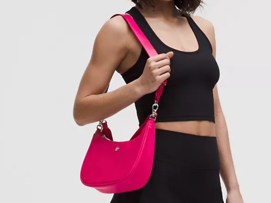 woman wearing a black tank top and skirt with a hot pink shoulder bag on her arm
