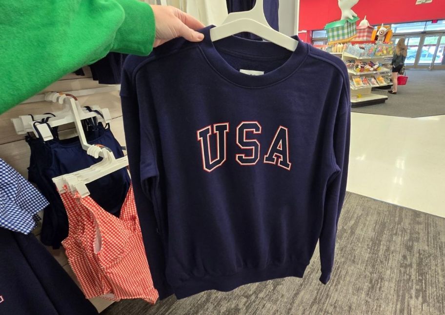 a womans hand holding a navy blue sweatshirt with a USA graphic on the chest