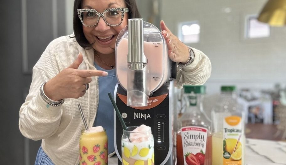 a woman points to a ninja slushi machine as she dispenses a frozen drink into a glass from the machine