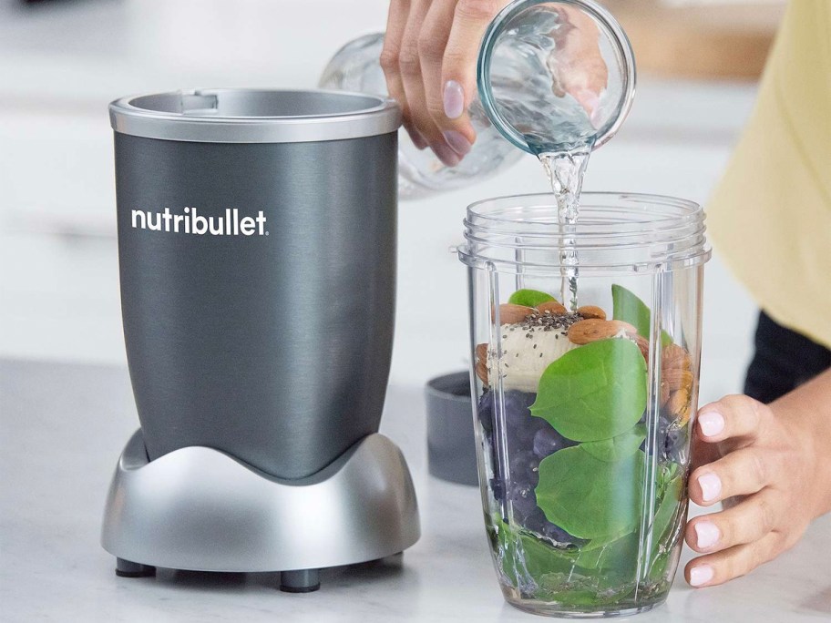 person putting veggies and water into blender cup 