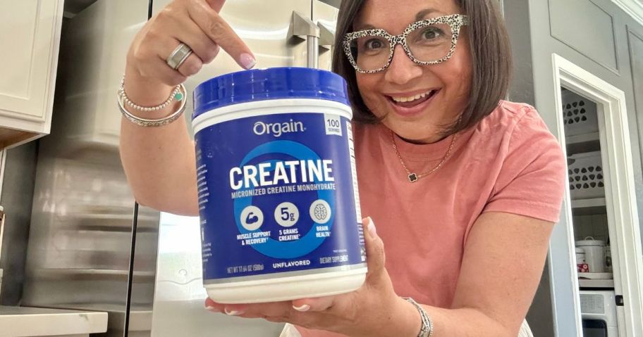 woman holding Orgain Creatine Monohydrate Micronized Powder 17.64oz tub and pointing to it