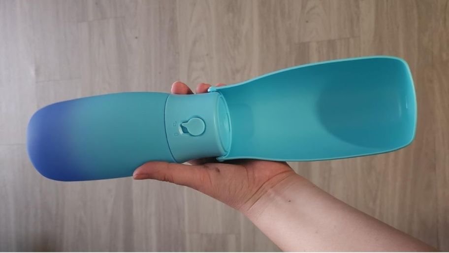 a womans hand holding an open portable dog water bottle