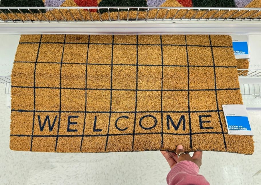 a womans hand holding a coir doormat with the word "welcome" on it