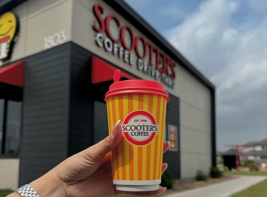 hand holding a to-go coffee cup in front of a Scooter's Coffee shop