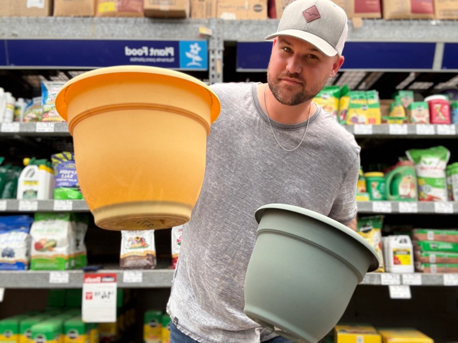 smiling man holding up two self watering plastic planters in a store aisle