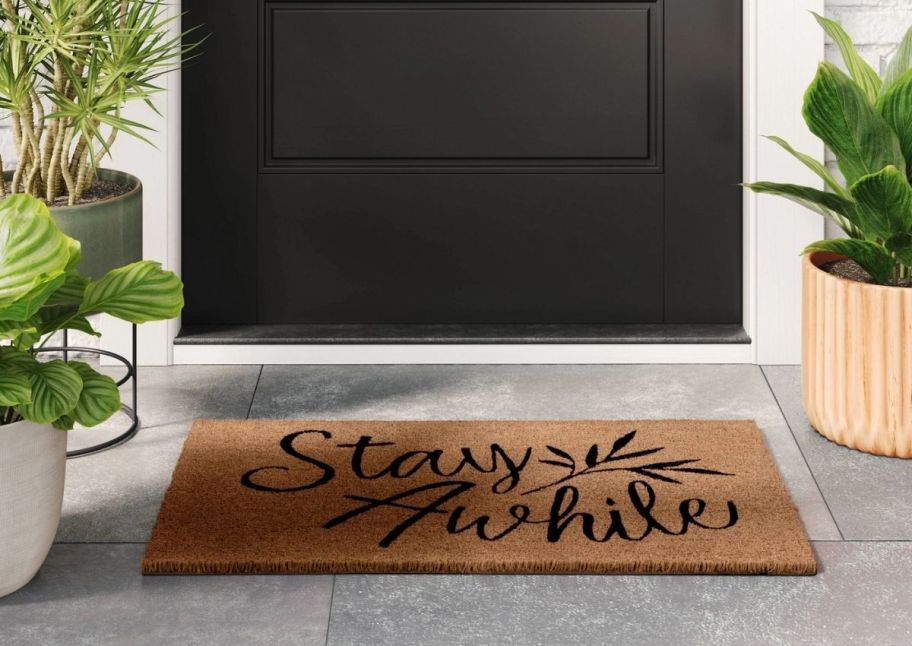 a coir doormat with a black text with words stay awhile on it infront of a white door