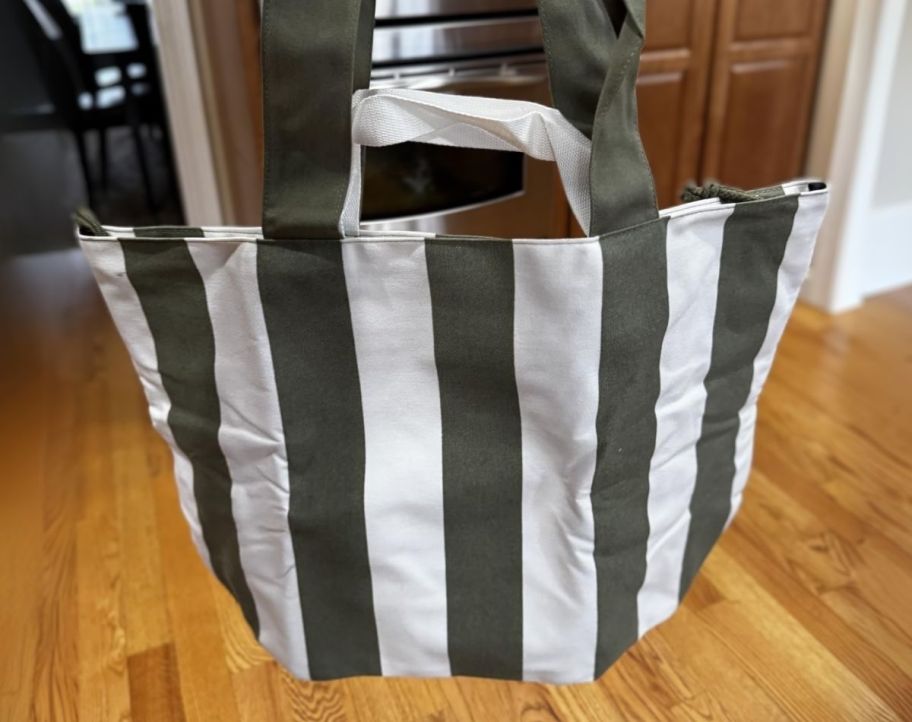 a hand holding out an olive green and white striped tote bag