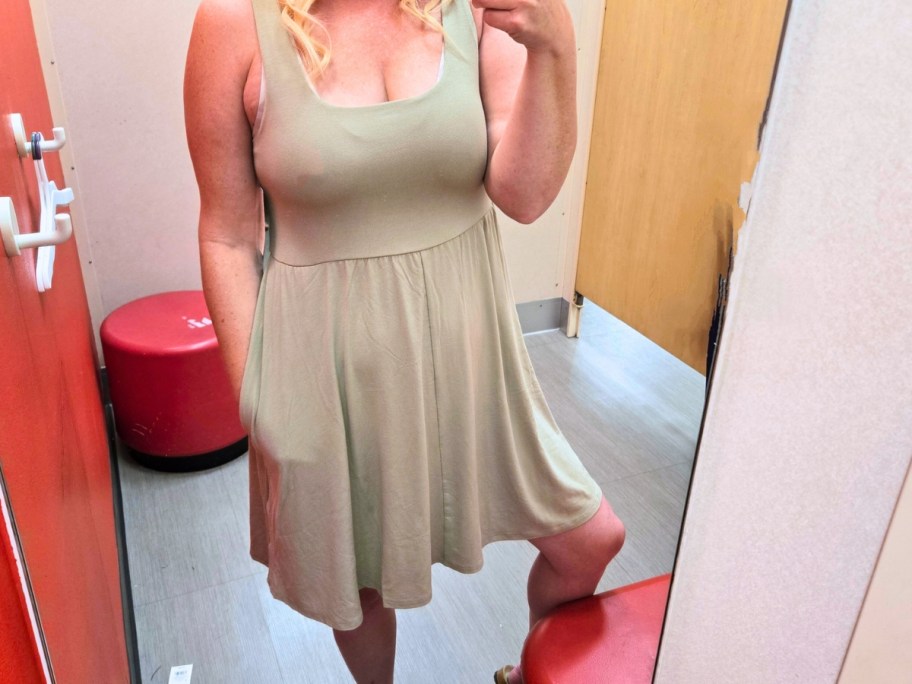 woman taking a selfie in a dressing room mirror wearing an olive green sleeveless dress