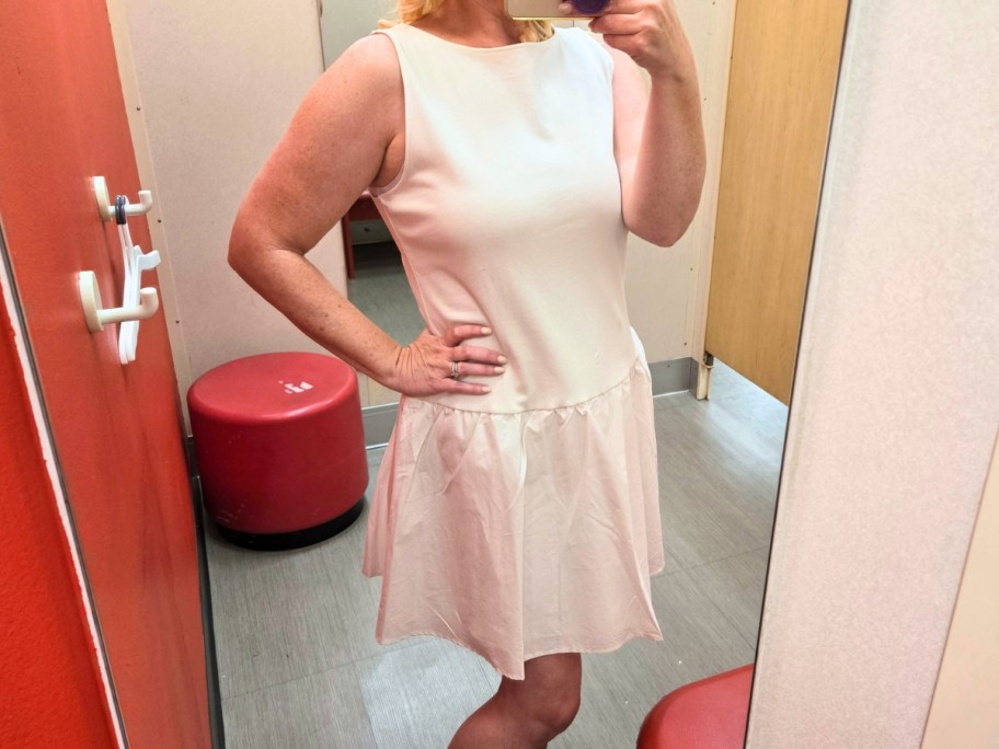 woman taking a selfie in a dressing room mirror wearing an off white sleeveless dress