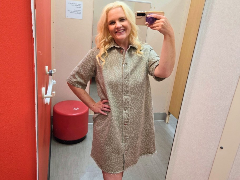woman taking a selfie in a dressing room mirror wearing a tan print button down shirt dress