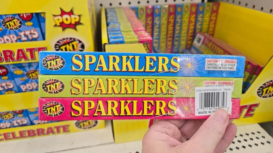 Colorful TNT brand sparklers in red, green, and blue packaging stacked on store shelf.
