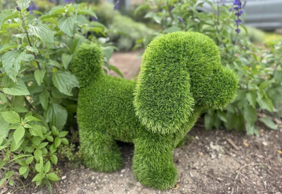 a green artificial grass turf dog next to a plant in a flowerbed
