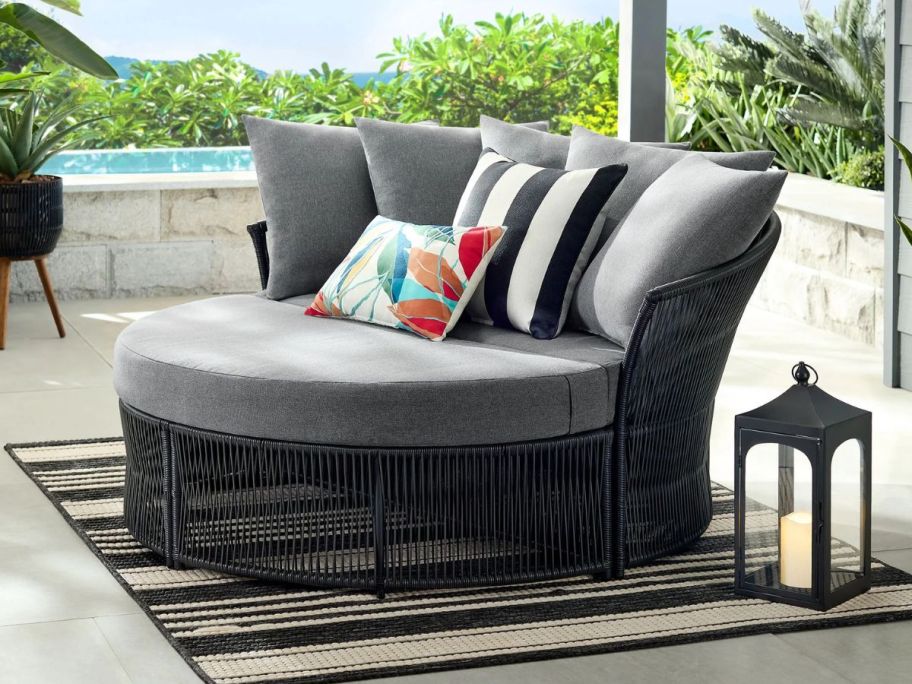The Mainstays Logan Outdoor Daybed wiith decorative throw pillows on it and a solar lantern set beside it