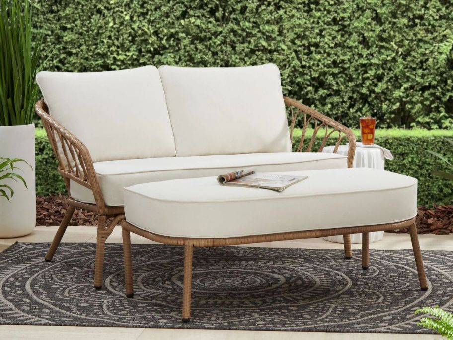 The Better Homes & Gardens Willow Sage Wicker Outdoor Loveseat & Ottoman  with cream color cushions on a patio